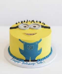 Minions Birthday Cake NYC with yellow buttercream, edible goggles, blue overalls, and custom birthday message by Crumbly.